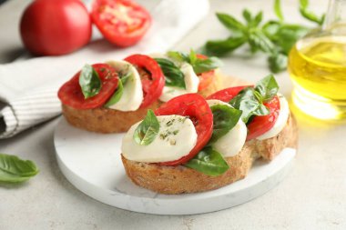 Mozarella peynirli lezzetli sandviçler, açık gri masada domates ve fesleğen, yakın plan.