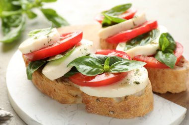 Mozarella peynirli lezzetli sandviçler, açık gri masada domates ve fesleğen, yakın plan.