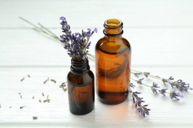 Lavanta yağı ve çiçekler beyaz ahşap masada, yakın plan.