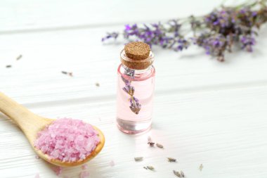 Lavanta yağı, çiçekler ve deniz tuzu beyaz ahşap masada, yakın plan.
