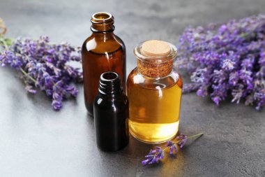 Şişelerdeki yağlar ve gri desenli masadaki lavanta çiçekleri, yakın plan.