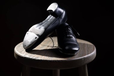 Siyah arka planda tahta taburede step dansı için bir çift ayakkabı, yakın plan.