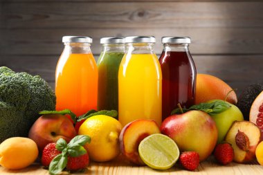 Cam şişelerdeki lezzetli sıvılar, taze malzemeler ve ahşap masa üzerindeki otlar kahverengi arka planda, yakın plan.