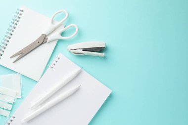 Açık mavi zemin üzerine beyaz defterler ve diğer kırtasiye malzemeleri, düz zemin. Metin için boşluk