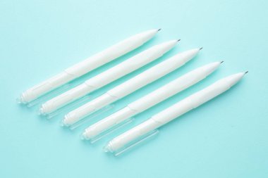 Açık mavi arka planda beyaz kalemler, düz uzanmış.