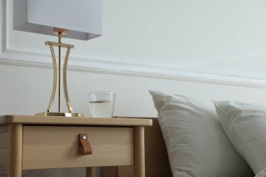 Yatak odasının yanında lamba ve bir bardak su olan komodinin yanında.