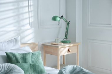 Yatak odasının yanında lamba ve bir bardak su olan komodinin yanında.