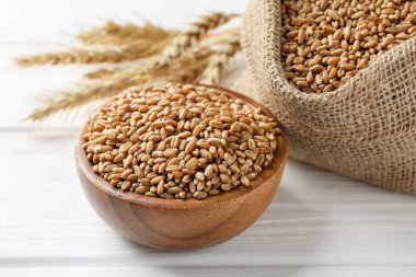 Kase içinde buğday taneleri, çuval bezi torbası ve beyaz ahşap masada çivili çubuklar, yakın plan.