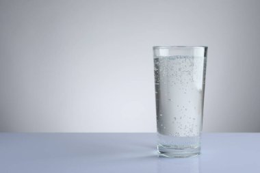 Açık gri gradyan arkaplana karşı beyaz masadaki cam bardakta soda tazeleniyor. Metin için boşluk