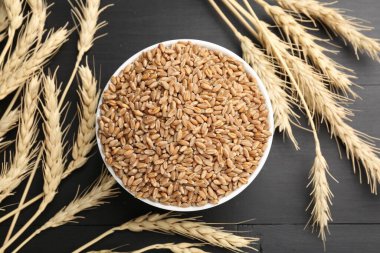 Kasede buğday taneleri ve siyah tahta masada çiviler, düz uzanmış.