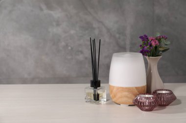 Gri duvarın yanındaki beyaz ahşap masada yanan mumlar ve aroma yağıyla spa kompozisyonu, metin için boşluk