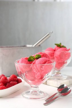 Tatlı kaselerinde naneli ahududu şerbeti, beyaz ahşap masada taze meyveler açık gri arka planda, yakın planda.