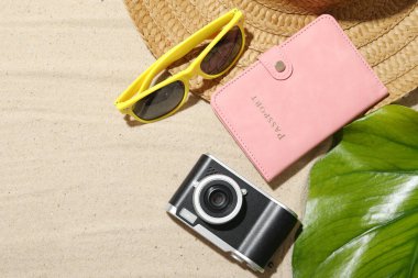 Yaz tatili zamanı. Kamera, pasaport, yeşil yaprak ve kumdaki plaj aksesuarları. Metin için boşluk