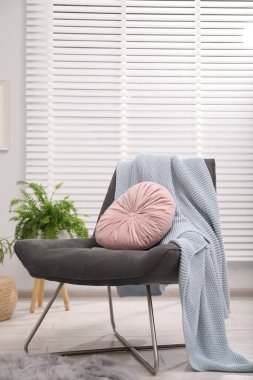 Oturma odasında pembe yastıklı ve battaniyeli rahat gri koltuk. İç tasarım