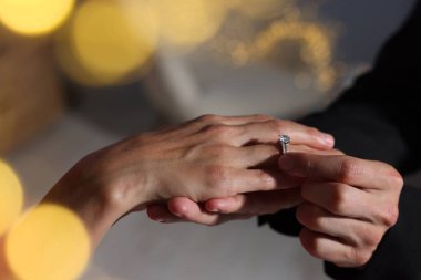 Evlilik teklifi yapıyor. Nişan yüzüğünü evde kız arkadaşının parmağına takan bir adam, yakın plan. Bokeh etkisi