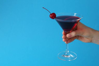 Açık mavi arka planda, kirazlı martini kokteyli tutan kadın, yakın plan. Metin için boşluk