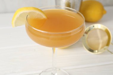 Bardakta limon dilimli martini kokteyli ve beyaz ahşap masada meyve, yakın plan.