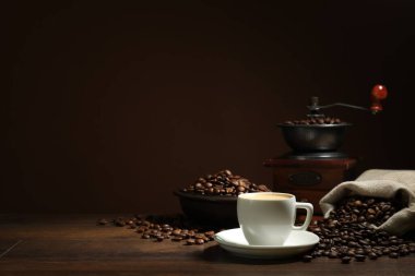 Kahverengi arka plan, kahve fincanı, fasulye ve öğütücü ahşap masa, metin için yer