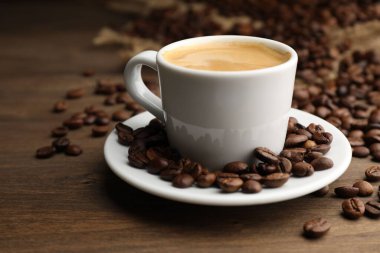 Aromatik kahve fincanda ve fasulyeler ahşap masada, yakın plan.