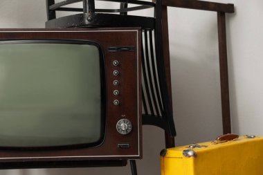 Retro TV, sandalyeler ve beyaz duvarın yanında sarı bavul. Kullanılmış eşyalar