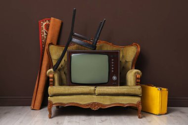 Kanepe, sandalye, bavul ve halı, kahverengi duvarın yanında. Kullanılmış eşyalar