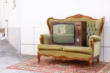 Dışarıdaki beyaz duvarın yanında kanepe ve halı üzerinde Retro TV. Kullanılmış eşyalar