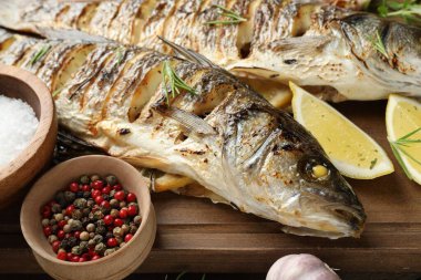 Ahşap masada biberiye ve limonla servis edilen lezzetli kavrulmuş deniz kabuğu balığı, yakından. Ev yapımı deniz ürünleri yemeği.