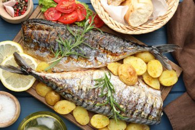 Baharat ve sebzelerle servis edilen kızarmış uskumrular mavi ahşap masada, düz yerde. Ev yapımı deniz ürünleri yemeği.