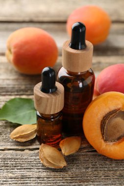 Gerekli yağ şişeleri, taze kayısılar, çekirdekler ve ahşap masada yeşil yaprak, yakın plan.