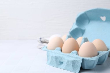 Yumurta kartonunda çiğ tavuk yumurtası, beyaz fayanslı masa, yakın plan. Metin için boşluk