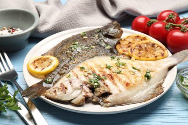 Açık mavi ahşap masada servis edilen limon dilimleri ve şifalı otlarla kızartılmış balık. Ev yapımı deniz ürünleri yemeği.