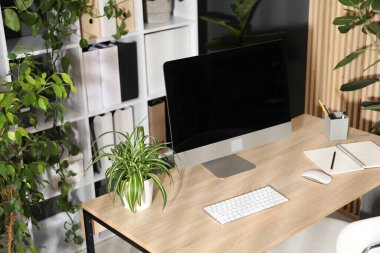 Modern bilgisayarı, kırtasiyesi ve çiçek dekoru olan şık bir iş yeri. Biyofilik iç tasarım