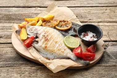 Patates, domates ve ahşap masada limon dilimleriyle servis edilen kızarmış balık. Ev yapımı deniz ürünleri yemeği.