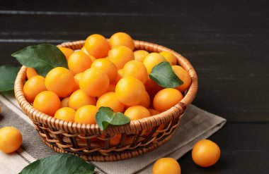 Olgun sarı kiraz erikleri ve koyu ahşap masada yapraklar, yakın plan.