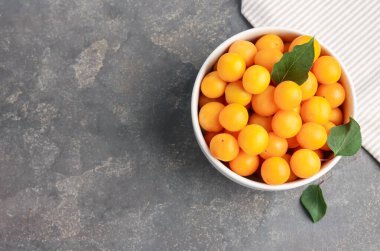 Olgun sarı kiraz erikleri ve yaprakları gri masanın üstünde, üst manzara. Metin için boşluk