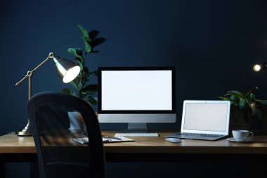 Ofisteki ahşap masa üzerinde modern bilgisayar, dizüstü bilgisayar ve kırtasiye malzemesi olan şık bir iş yeri.