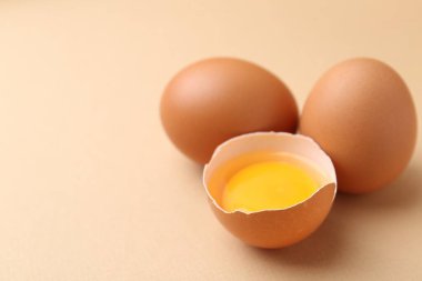 Bej arka planda tam ve kırılmış tavuk yumurtaları, yakın plan. Metin için boşluk