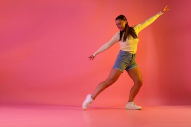 Gülümseyen kadın pembe arka planda neon ışıklarla dans ediyor. Metin için boşluk