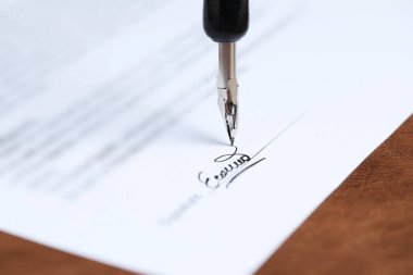 Kahverengi deri yüzeyinde dolma kalemle noter belgesi imzalanırken, yakın plan