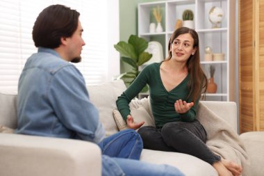 Kadın ve erkek evdeki kanepede konuşuyor.