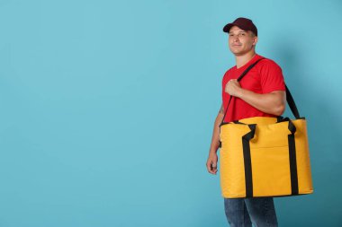 Açık mavi arka planda termo çantalı kurye, mesaj için boşluk. Yemek dağıtım servisi.