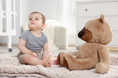 Küçük şirin bebek odada oyuncak ayıyla oynuyor.