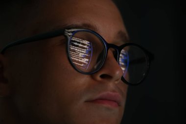 Siyah arka planda yansıması olan gözlüklü genç adam, yakın plan.