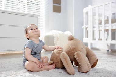 Küçük şirin bebek odada oyuncak ayıyla oynuyor.