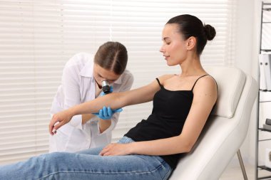 Doktor hastanede dermatoskopla genç kadının benini inceliyor.