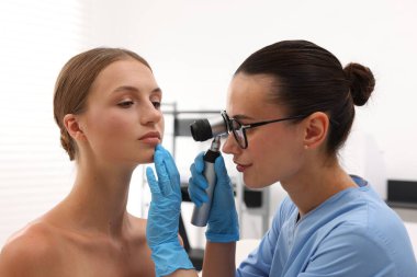 Doktor hastanede dermatoskopla genç kadının benini inceliyor.