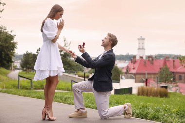 Nişan yüzüğüyle gülümseyen bir adam dışarıda sürpriz kız arkadaşına evlenme teklif ediyor.