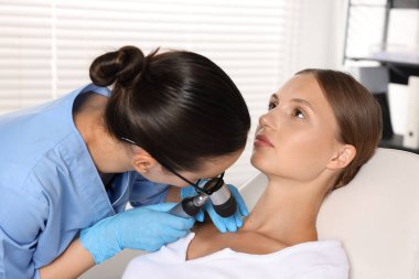 Doktor hastanede dermatoskopla genç kadının benini inceliyor.