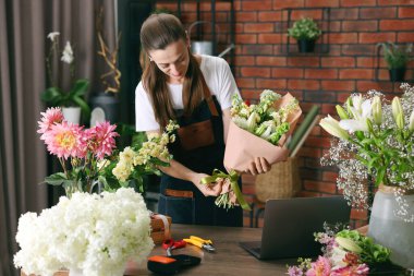 Profesyonel çiçekçi dükkandaki ahşap masada çiçek buketi yapıyor.