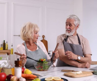 Yaşlı çift mutfaktaki mermer masada birlikte yemek pişiriyor.